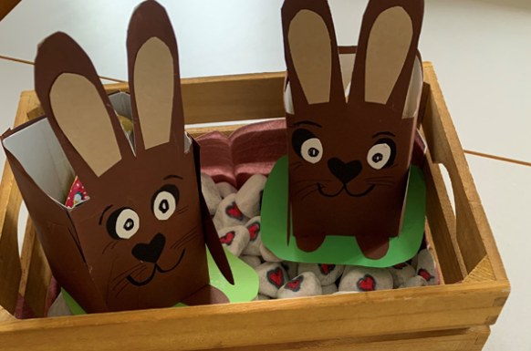 Zwei gebastelte Papposterhasen sitzen in einer Holzkiste und fungieren als Osternest