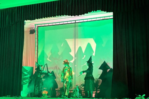 Eine grün beleuchtete Bühne mit Schülern präsentieren Szene aus Theaterstück
