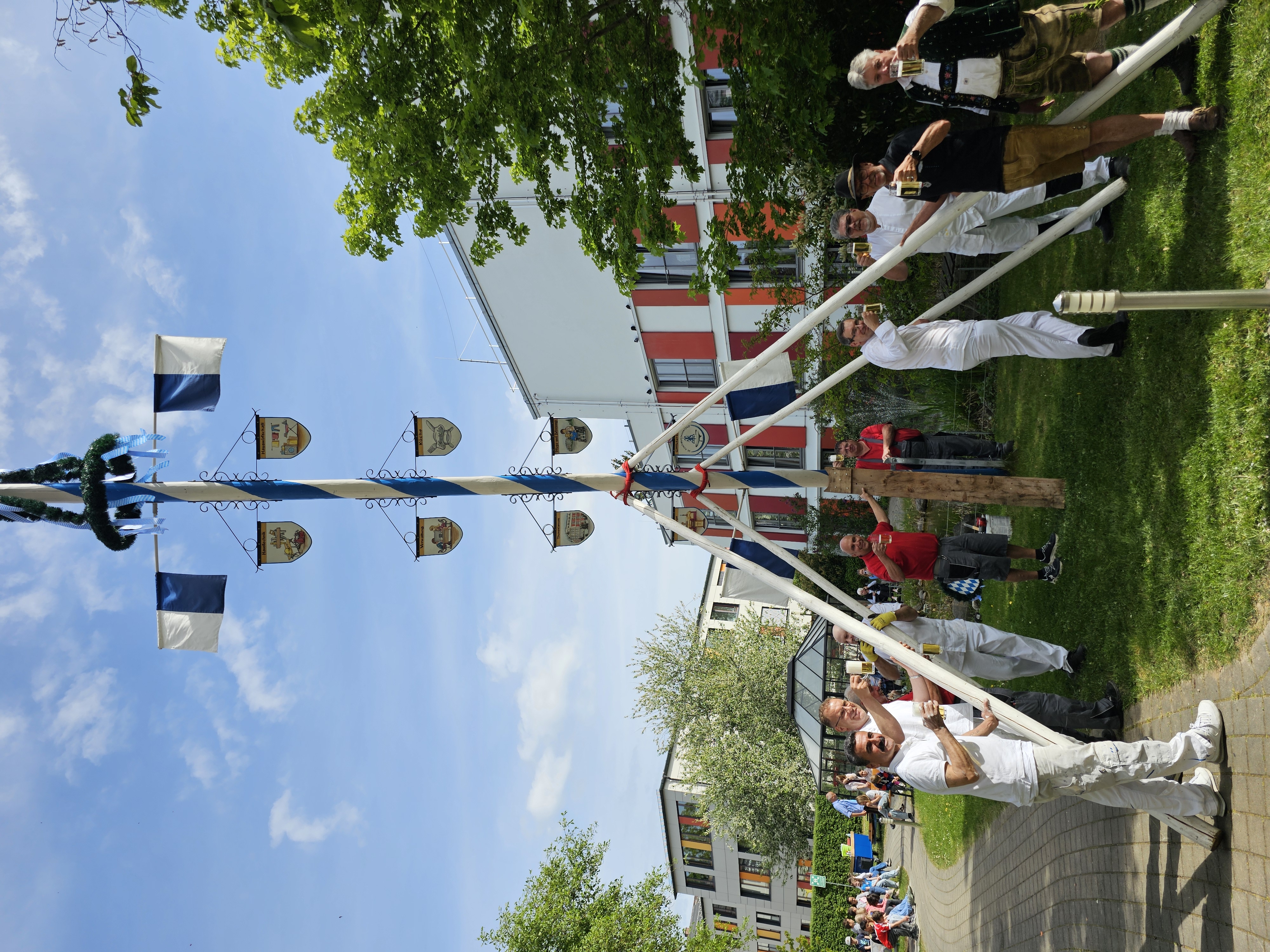 Der Maibaum wurde per Manneskraft aufgestellt, alle beteiligten Helfer gönnen sich ein Bier. Der Maibaum steht im Garten des Theresianums.